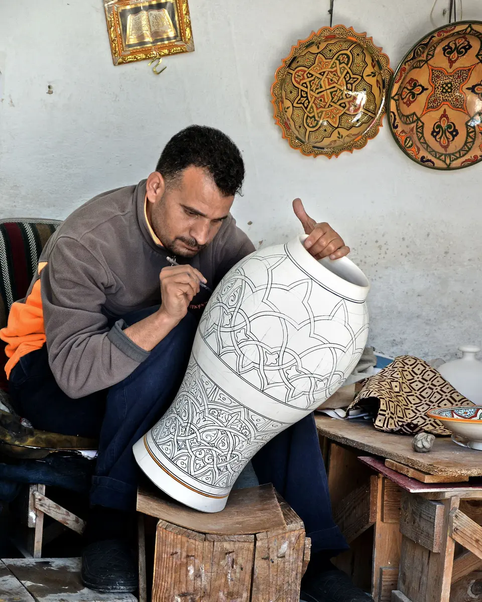 An artisan hand-painting the decoration of a large white vase